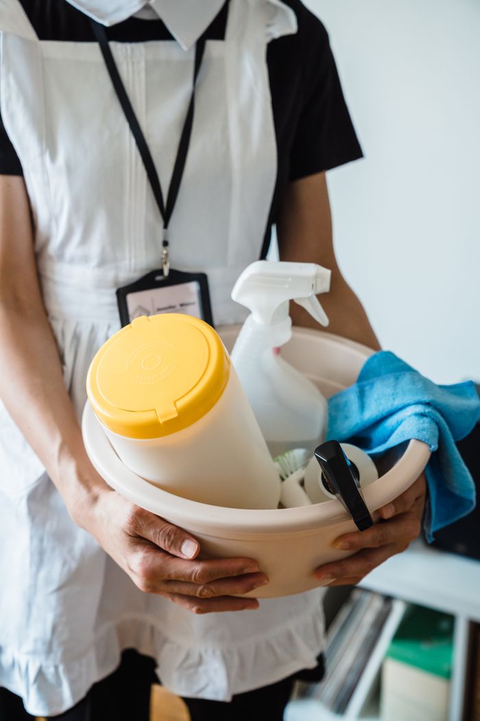 services-03 A uniformed cleaner holding a basin with cleaning supplies indoors. Ideal for cleaning and sanitation themes.